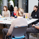 Menschen sitzen am Tisch bei einem Vortrag.